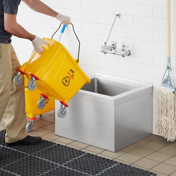 A man using a yellow container to clean a floor mop sink.