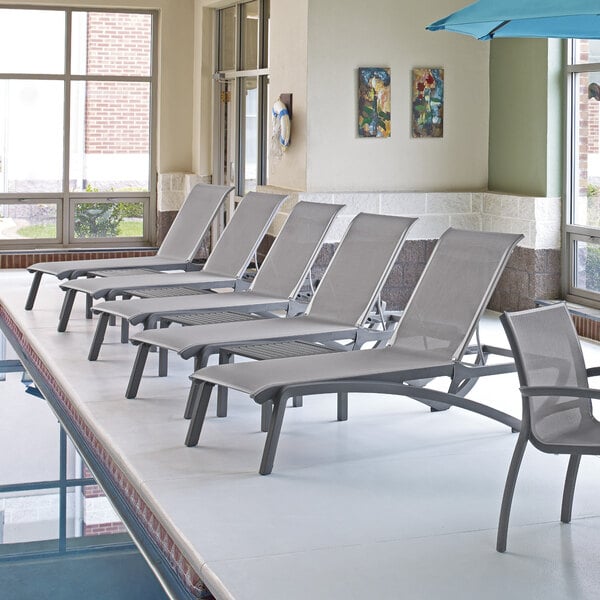 A row of Grosfillex Sunset Platinum Gray chaise lounge chairs with solid gray sling seats.