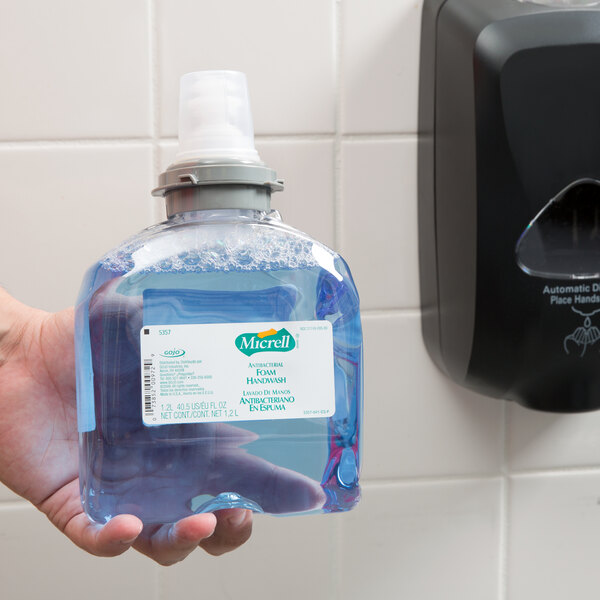 A hand holding a Micrell TFX floral antibacterial foaming hand soap bottle.