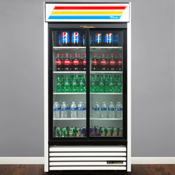 A True refrigerated glass door merchandiser with bottles of soda and water.