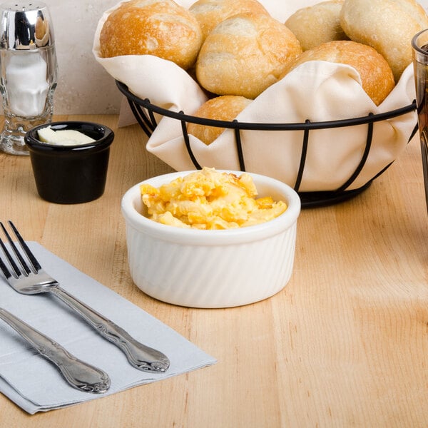 A table with a bowl of scrambled eggs and bread with a fork and knife on a napkin.