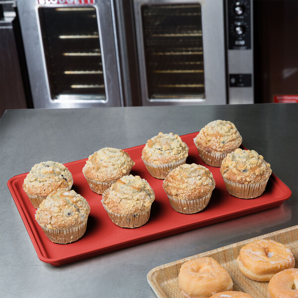 A red MFG Fiberglass Display Tray holding muffins on a counter.