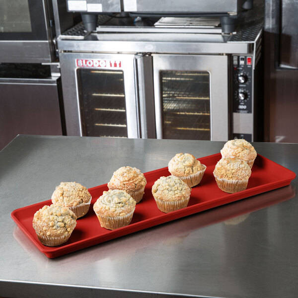 A red MFG Tray with muffins in paper wrappers on a counter.