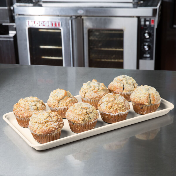 A beige MFG Tray supreme display tray holding muffins on a counter.
