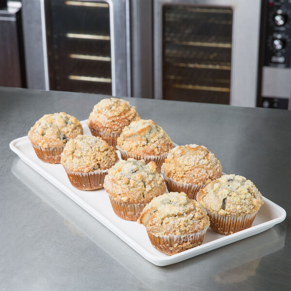 A MFG Tray white fiberglass market tray holding muffins on a table in a bakery display.