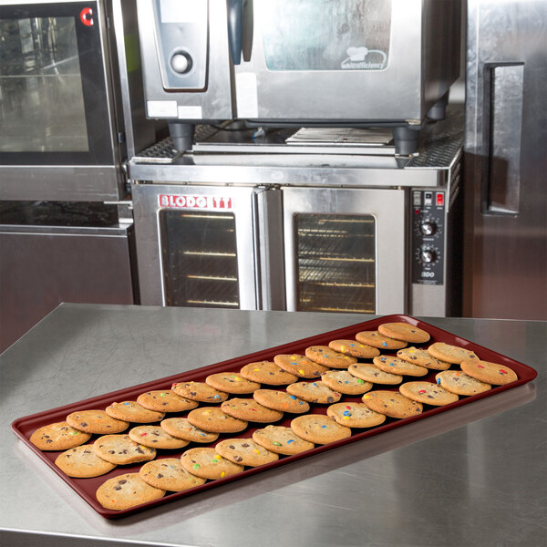 A burgundy MFG Tray bakery display tray with cookies on a kitchen counter.