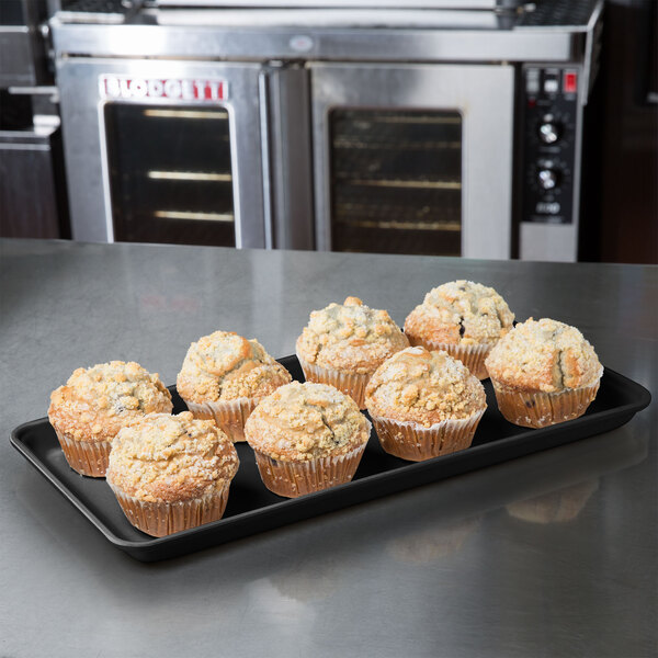 A black MFG Tray supreme display tray holding muffins on a counter.