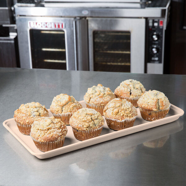 A MFG Tray peach fiberglass display tray of muffins on a counter.