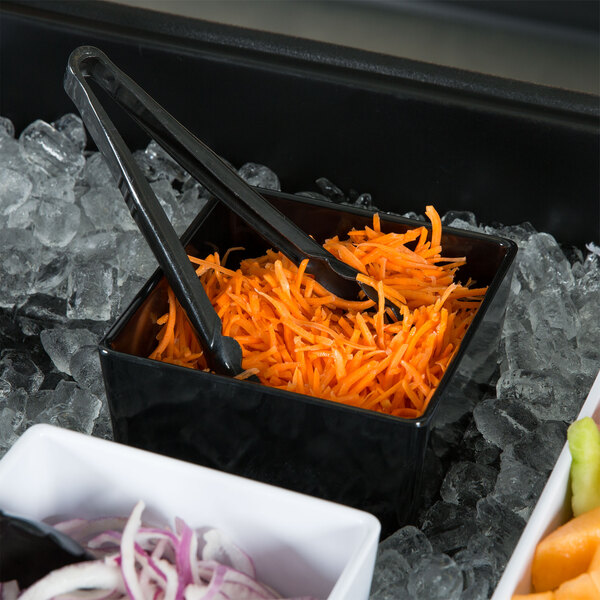 A black Tablecraft melamine bowl containing shredded carrots on a salad bar counter.