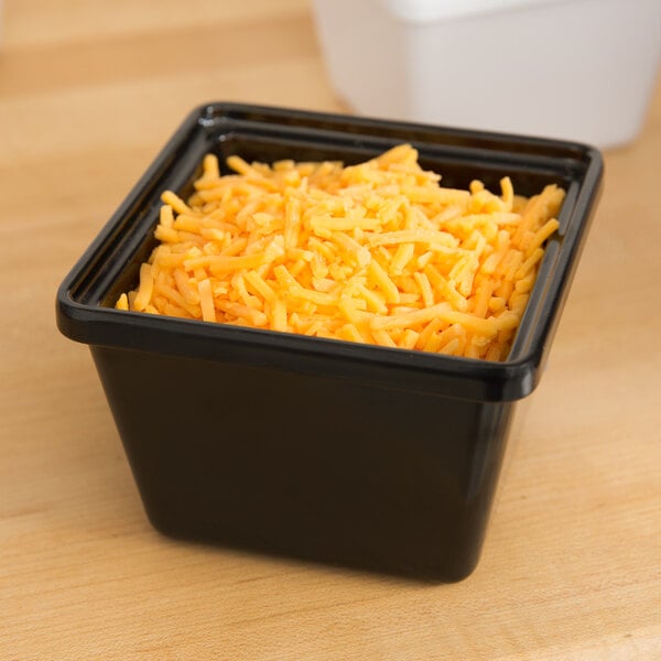 A black GET square melamine crock filled with shredded cheese on a table.