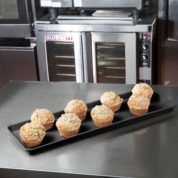 A black MFG Tray Supreme Display Tray holding muffins on a counter.
