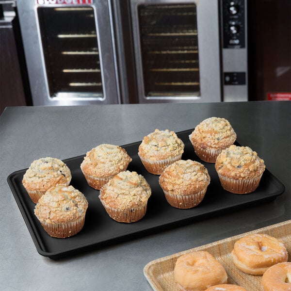 A black MFG Fiberglass Supreme Display Tray of muffins on a bakery counter.