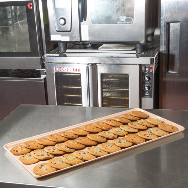 A MFG Tray peach fiberglass supreme display tray of cookies on a counter in a bakery display.