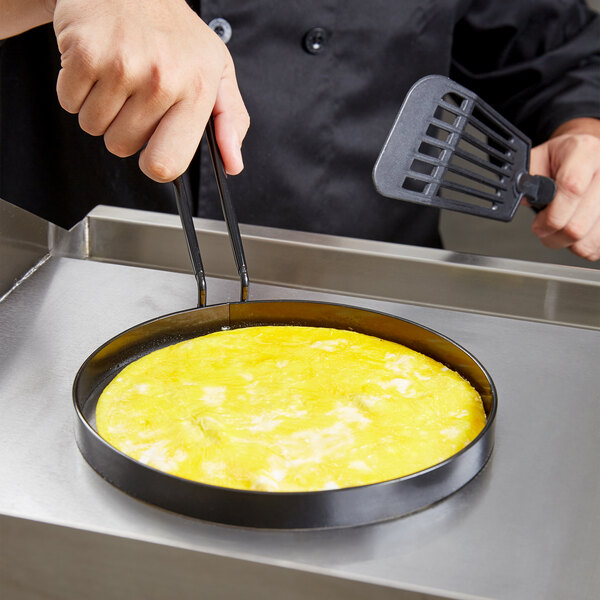 A person using a Tablecraft non-stick egg ring to cook an omelette in a pan.