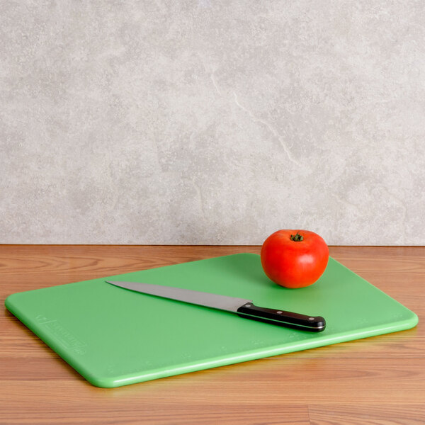A San Jamar green cutting board with a tomato and a knife.