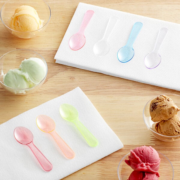 Assorted neon plastic taster spoons on a white surface with bowls of ice cream.
