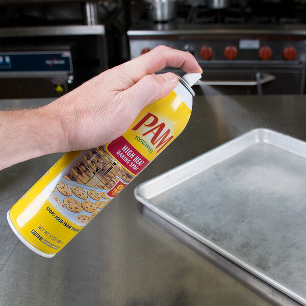 A hand sprays PAM High Heat Baking Release from a can onto a baking tray.