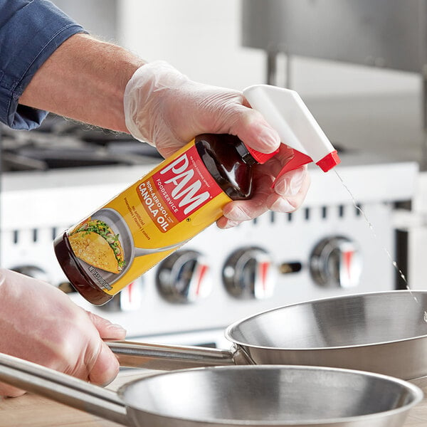 A person using PAM All Purpose Liquid Release Spray to pour liquid into a silver pan.