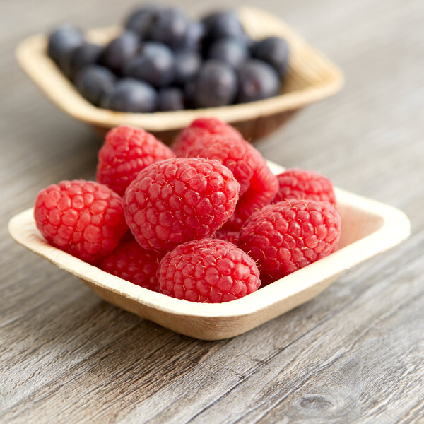 A  EcoChoice square palm leaf bowl filled with raspberries and blueberries on a table.