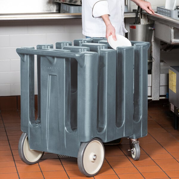 A chef in a white coat places a white plate in a grey Cambro dish dolly.