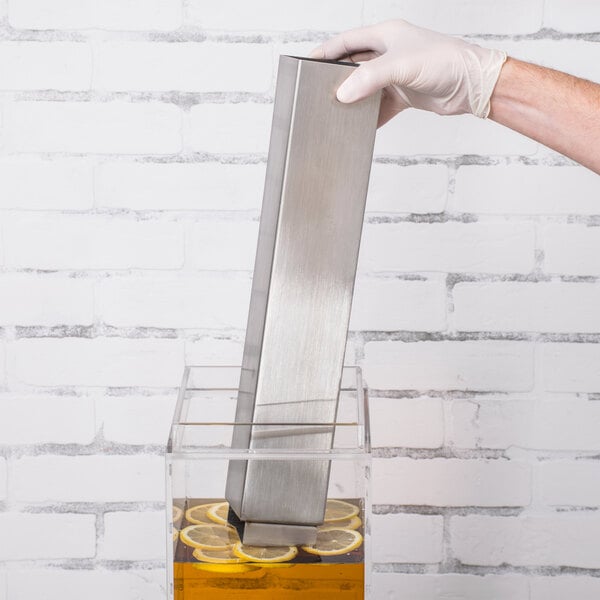 A gloved hand placing a stainless steel ice chamber into a container of liquid.