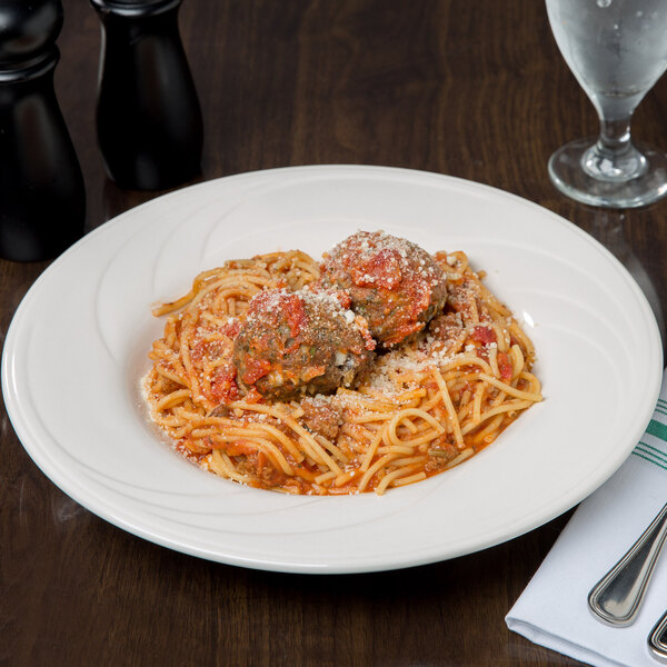 A Libbey ivory porcelain pasta bowl filled with spaghetti and meatballs on a table.
