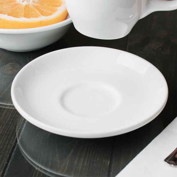 A close up of a Libbey Reflections white porcelain tea saucer with a slice of orange on it.