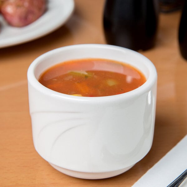 A white Libbey porcelain bouillon cup filled with soup on a table.
