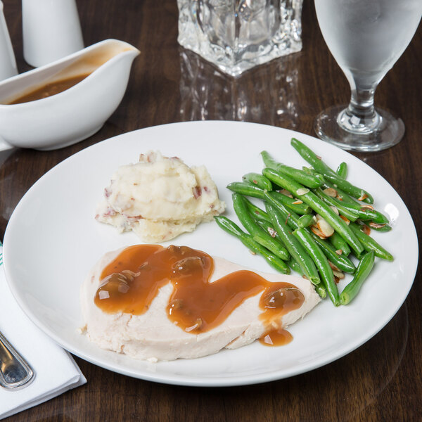A Libbey Aluma White Porcelain Coupe plate with turkey, mashed potatoes, gravy, and green beans on a table.