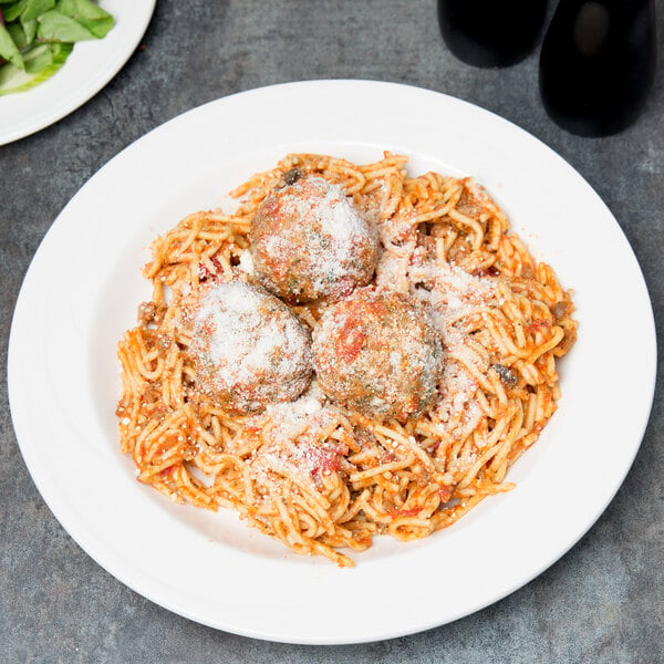 A Libbey ivory porcelain bowl filled with spaghetti and meatballs with cheese on top.