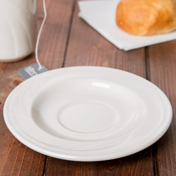 A Libbey ivory porcelain tea saucer on a table with a tea cup.