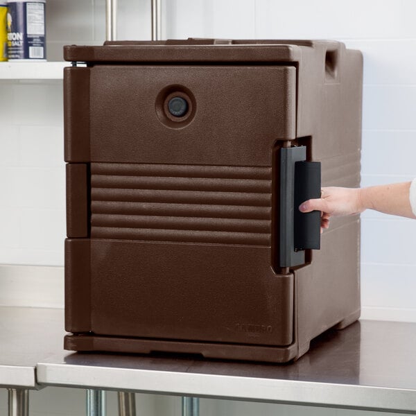 A person opening a brown Cambro Ultra Pan Carrier with black handles.