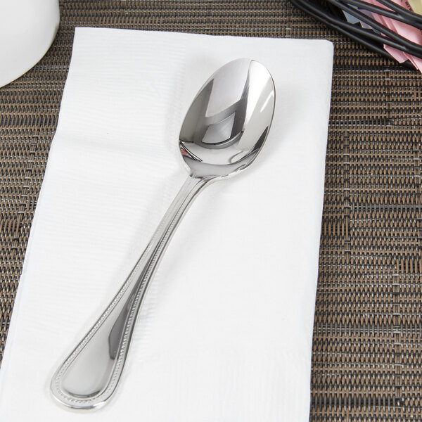 A Libbey stainless steel European teaspoon on a napkin next to a cup.