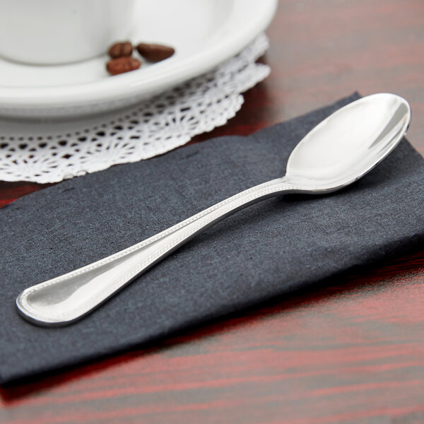 A stainless steel Libbey Calais demitasse spoon on a napkin next to a cup of coffee.