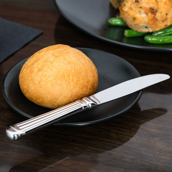 A black plate with a roll and a Libbey Aegean stainless steel bread and butter knife.