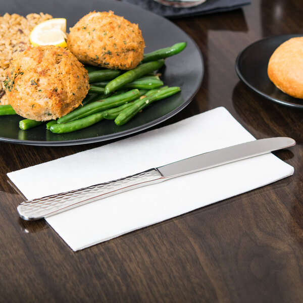 A Libbey stainless steel dinner knife with a fluted blade on a white table next to a plate of food.