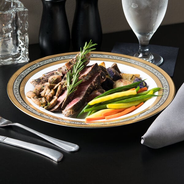A 10 Strawberry Street Elegance porcelain dinner plate with meat and vegetables on it, with a fork and knife on the table.