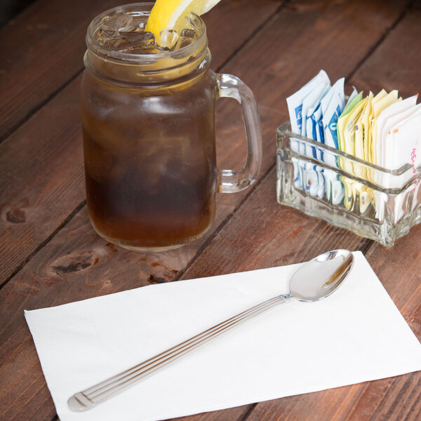 A glass mug of iced tea with a lemon slice in it and a Libbey stainless steel iced tea spoon in a glass dish.
