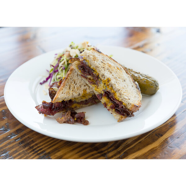 A sandwich with bacon and pickles on a 10 Strawberry Street Bistro porcelain dinner plate.