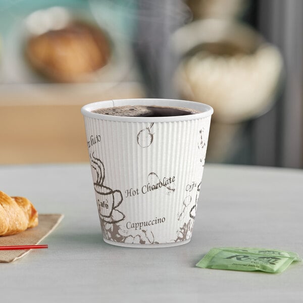 A close-up of a Choice double wall paper hot cup with a bean print filled with coffee on a table with a croissant.