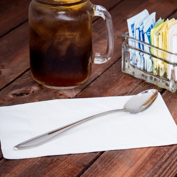 A World Tableware stainless steel iced tea spoon on a napkin next to a glass jar of tea.