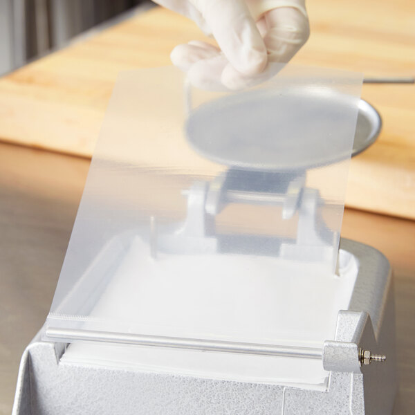 A hand in a glove holding a Garde Hamburger Patty paper sheet over a food processor.