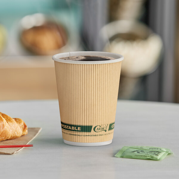 A close-up of an EcoChoice Double Wall Kraft paper hot cup full of coffee on a table with a croissant.