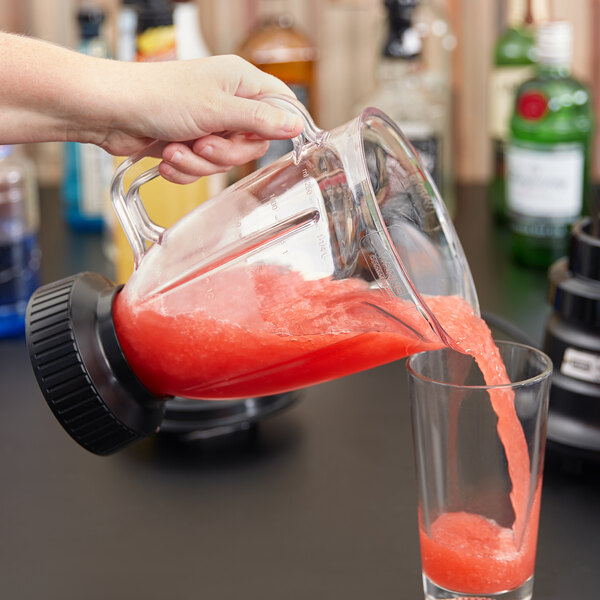 A person pouring a red liquid from a green Waring blender jar into a glass.