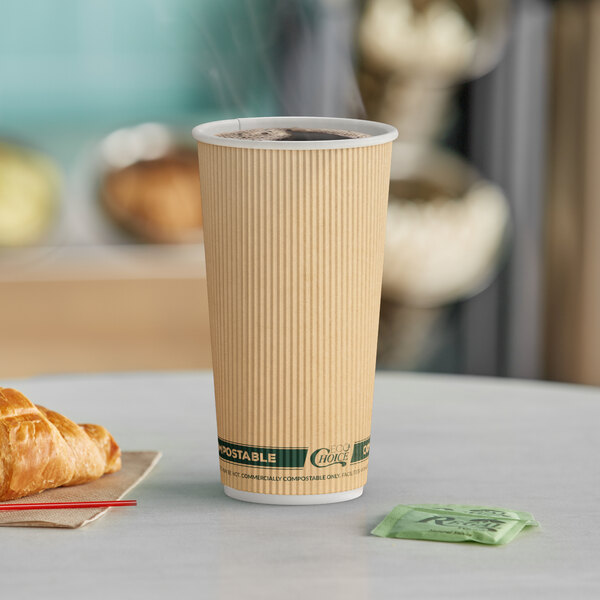 A close-up of a EcoChoice Double Wall Kraft Compostable Paper Hot Cup full of coffee on a table with a croissant.