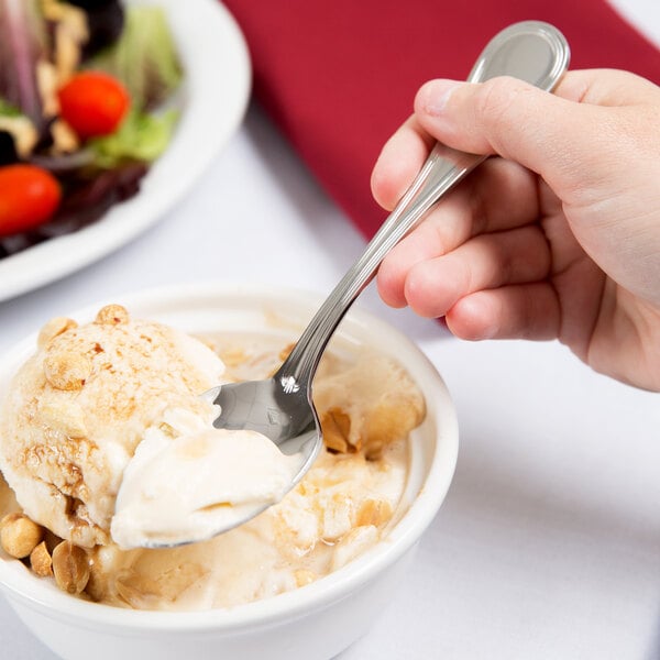 A hand holding a Libbey Geneva stainless steel dessert spoon over a bowl of ice cream.