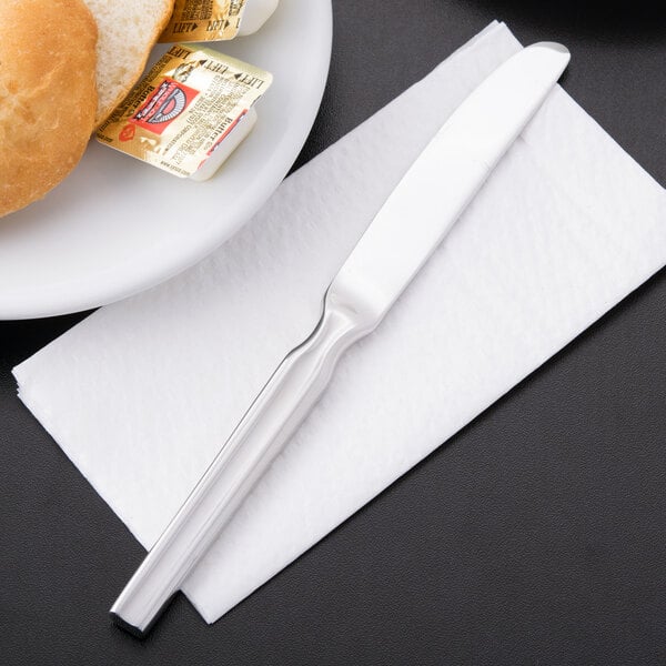 A Libbey stainless steel bread and butter knife on a napkin next to a plate of bread.