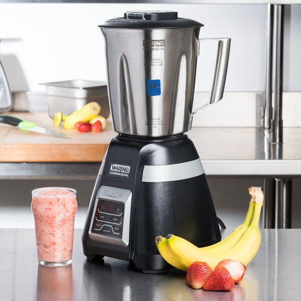 A Waring bar blender on a counter with a banana and strawberries.