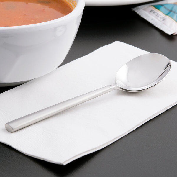 A white napkin with a Libbey Cimarron bouillon spoon next to a bowl of soup.