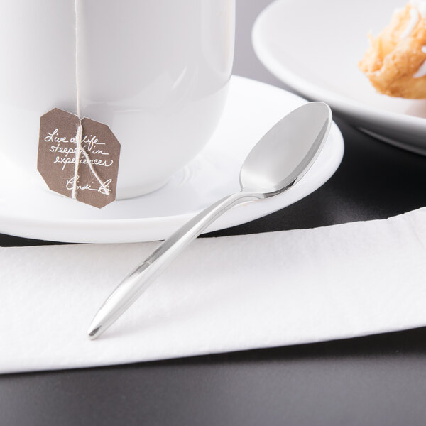 A Libbey stainless steel demitasse spoon on a plate with a tea cup.